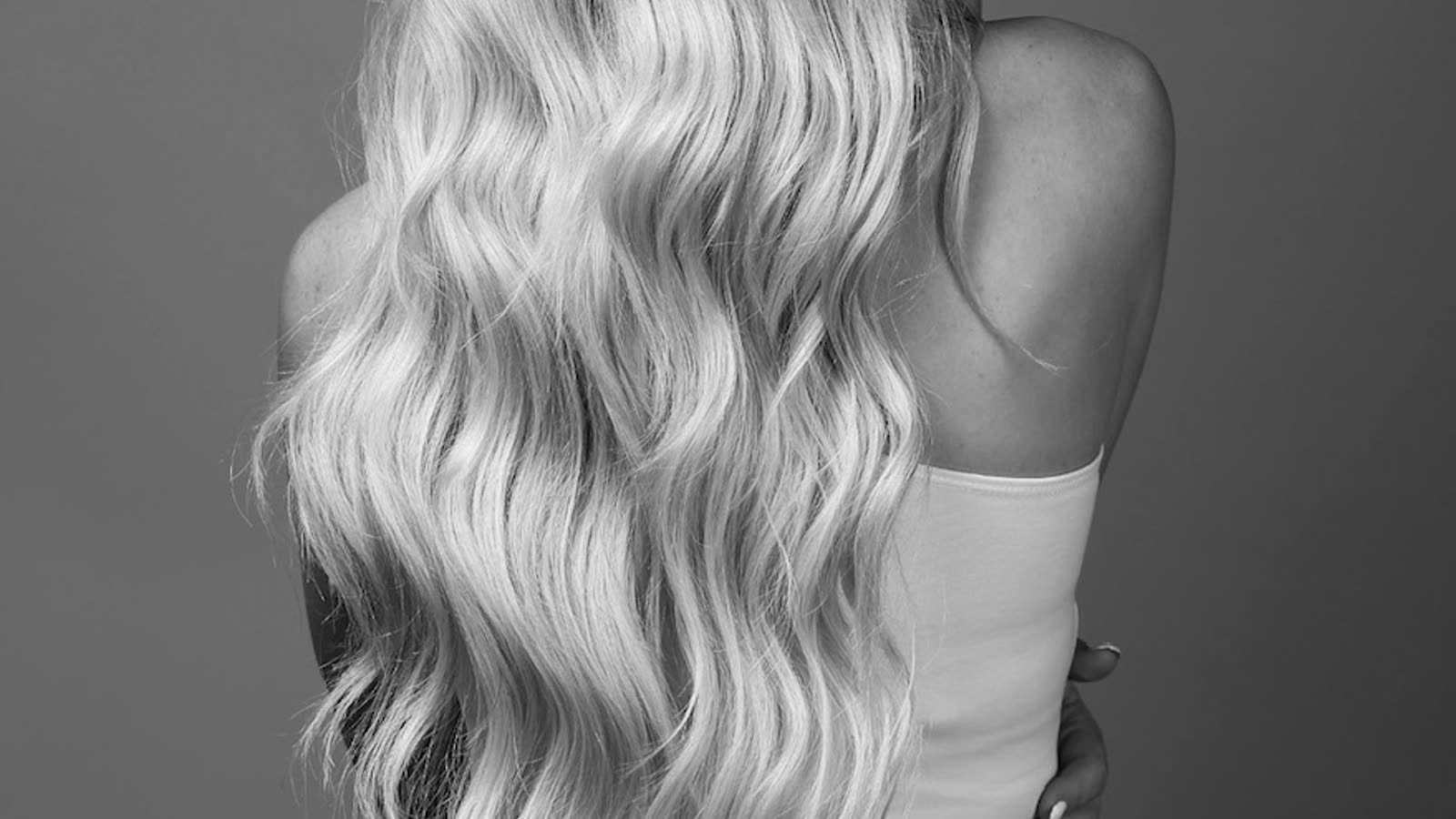 Long blonde tape-in extensions in loose waves, cropped wide from behind